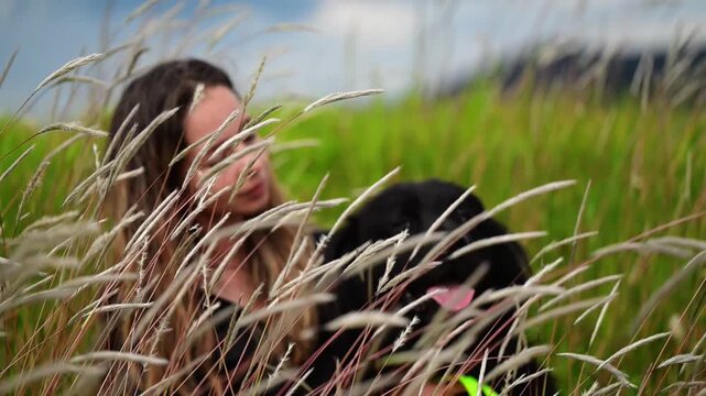 Horizontal video in Slow motion  1080p at 60 fps of a happy girl sitting in the tall grass with her beautiful black dog, both enjoying their time together
