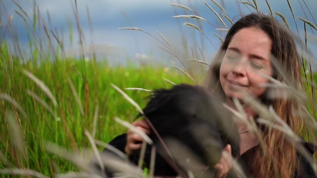 Horizontal video in Slow motion 1080p at 60 fps of a happy girl sitting in the tall grass with her beautiful black dog, both enjoying their time together
