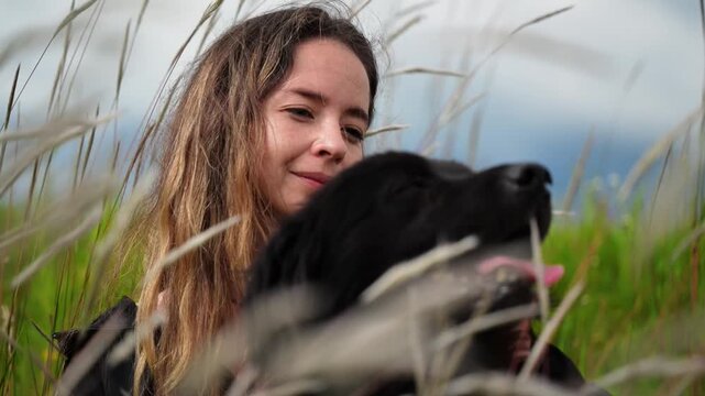 Horizontal video in Slow motion 1080p at 60 fps of a happy girl sitting in the tall grass with her beautiful black dog, both enjoying their time together
