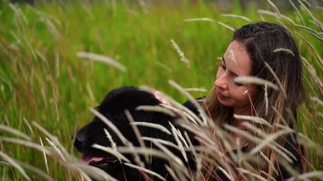 Horizontal video in Slow motion 1080p at 60 fps of a happy girl sitting in the tall grass with her beautiful black dog, both enjoying their time together
