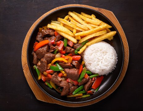 delicious peruvian beef lomo saltado with stir fried vegetables fries and rice in black pan overhead shot