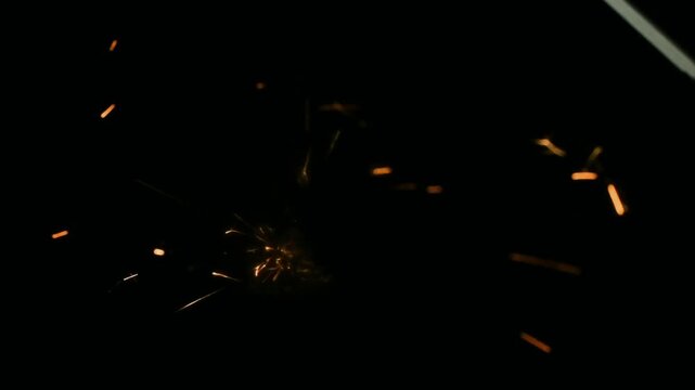 Small orange sparks scattering over dark backdrop gentle particle motion suggesting subtle metal abrasion and micro fragments