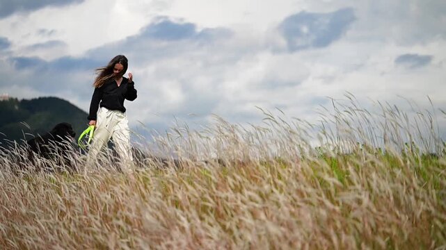 Horizontal video in slow motion at 1080p at 60 fps of a happy girl walking through long grass with her beautiful black dog
