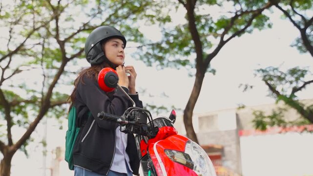 Early in the clip, a young woman near the center of the frame lifts a black helmet onto her head beside a red motorcycle