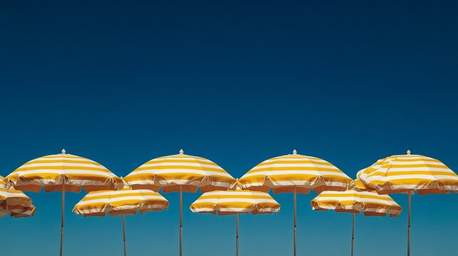 Bright yellow and white striped beach umbrellas stand against a clear deep blue sky on a sunny summer vacation day
