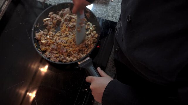 Chef cooking minced meat and mushrooms in frying pan