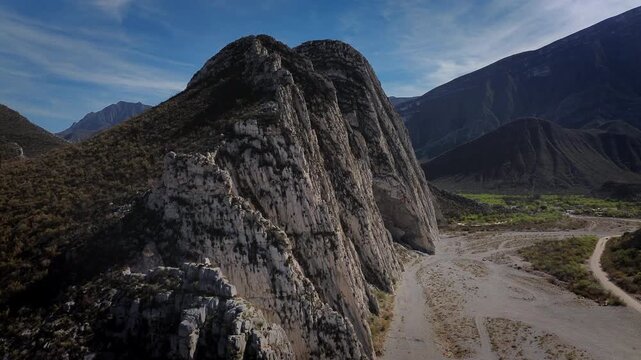 Aerial drone slowly reveals the rugged Huasteca Canyon landscape in Monterrey, with the dry Santa Catarina River basin cutting between dramatic arid mountain ranges and distant forests under a vivid b