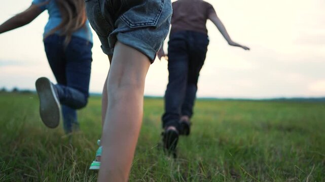 Children running on green grass field. Kids run together with arms spread wide. Happy children play outdoors at sunset. Kids enjoy freedom on open field. Group of children running on summer meadow.