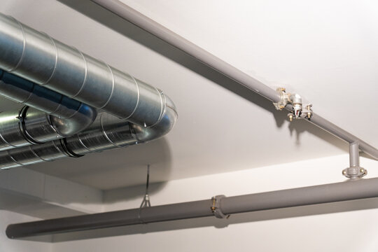 Exposed metal HVAC ventilation ducts and sprinkler pipes on a white ceiling. Modern industrial architecture.