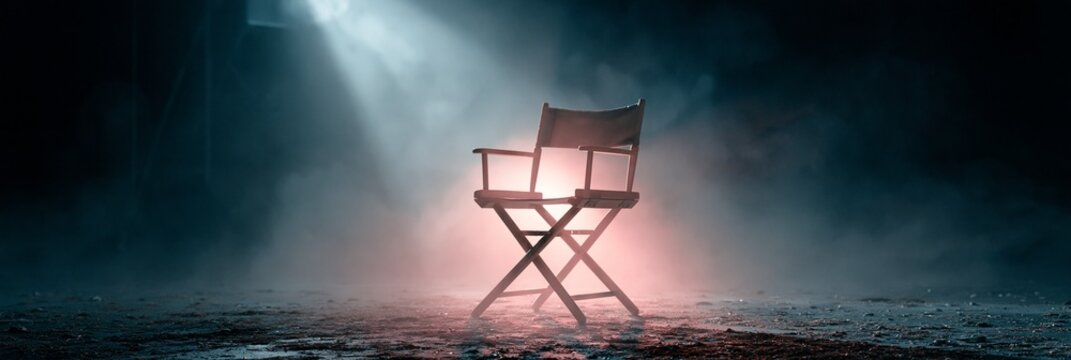 An empty director&acirc;&euro;&trade;s chair on a vintage film set, spotlight cutting through dusty air, nostalgic and respectful mood, low-key lighting, centered composition with soft background bokeh.
