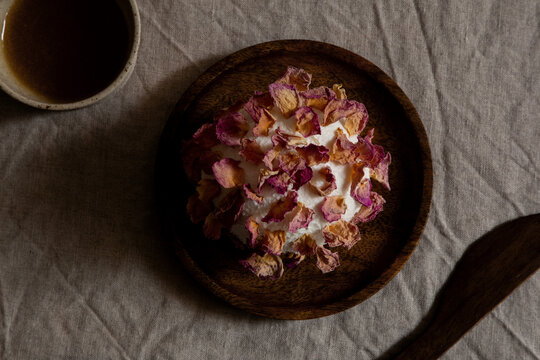Goat cheese sphere decorated with dried rose petals served on a wooden plate on linen tablecloth.