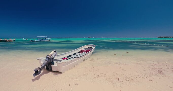 Small motorboat with outboard motor moored on a tropical white sand beach next to turquoise water