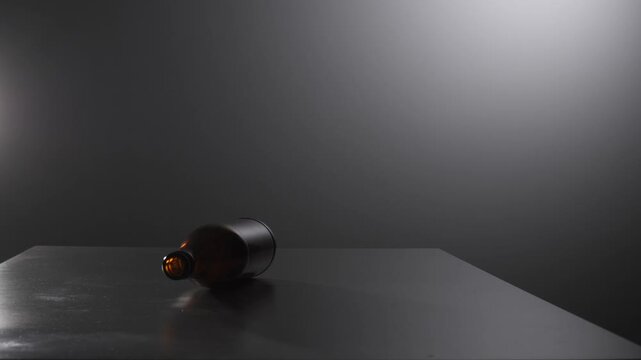 Empty dark amber glass bottle lying on its side on a flat dark gray surface, capturing a minimal still life with a subtle gradient background and soft lighting