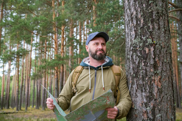 Obraz premium tourist with backpack holds paper map and enjoys peaceful moment in pine forest during hike. Nature appreciation and outdoor recreation concept