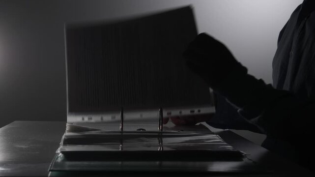 Man in silhouette sitting at a desk, reviewing important or secret report files in a binder, creating a sense of privacy, investigation, or clandestine work