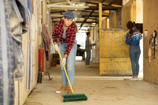 Girl cleans the floor of a stable with a fetlock