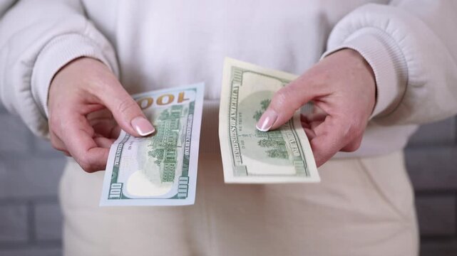 Woman comparing old and new one hundred dollar bills. Close-up of female hands holding and comparing two types of one hundred dollar bills, showing the difference between the old design and the newer
