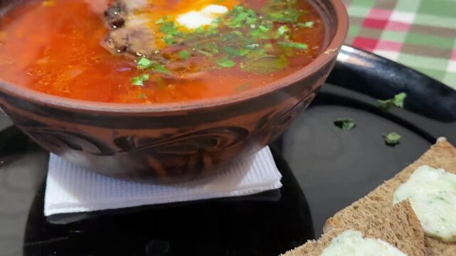 Traditional Ukrainian borscht with sour cream herbs black bread and pork fat on checkered tablecloth