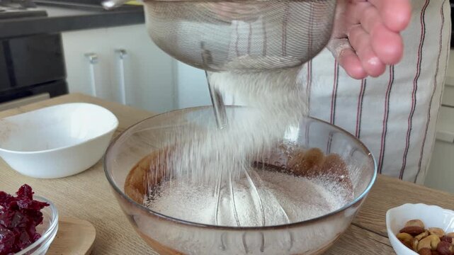 A woman sifts flour through a sieve into a glass bowl with dough. Home cooking