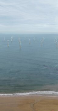 Portrait aerial drone footage of offshore wind turbines near Redcar and Middlesbrough on the North East coast of England with sandy beach gentle waves coastal waters sandy beach and renewable energy