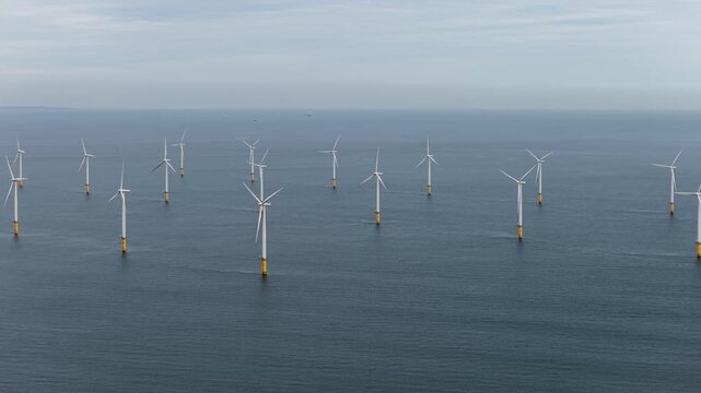 Aerial drone footage of offshore wind farm near Redcar Middlesbrough UK showing multiple turbines in the sea with distant coastline visible across calm water in a wide landscape scene