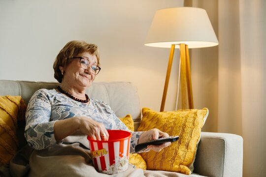 Senior woman enjoying popcorn watching tv at home