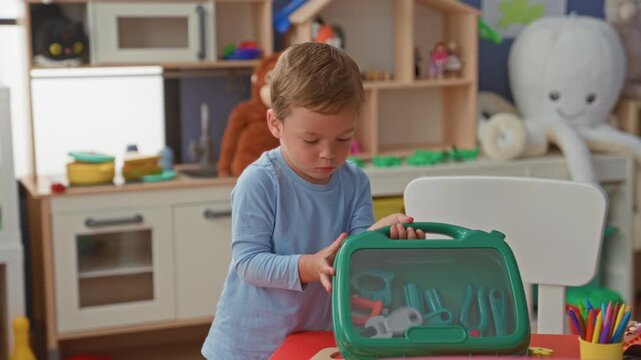 Boy opening a green toy case with hand at a playroom table in a building; concentration childhood play.