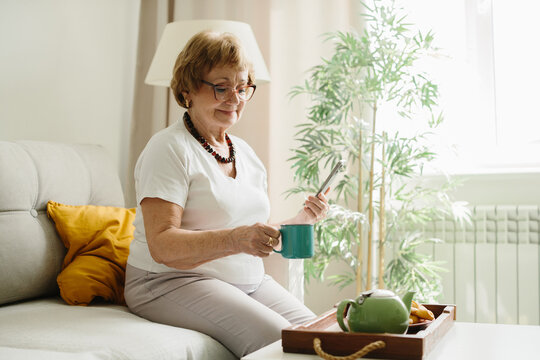 Senior woman using smartphone enjoying tea on sofa