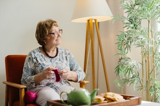 Happy senior woman knitting, enjoying leisure at home
