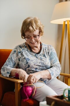 Happy senior woman knitting colorful yarn at home