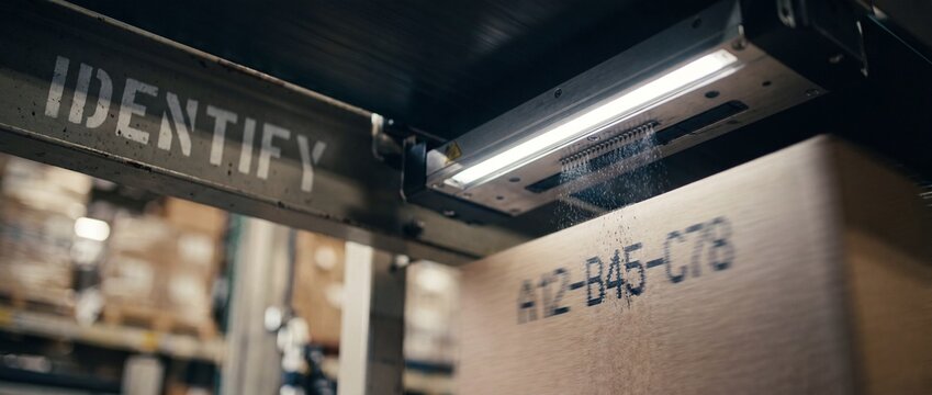 Industrial conveyor belt inkjet printer marking cardboard box on automated warehouse packaging line, scanning identification code for smart logistics, supply chain distribution, and manufacturing flow