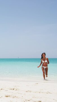 Vertical video beach travel vacation concept. Happy Asian American girl having fun on beach on luxury island. Mixed race woman.