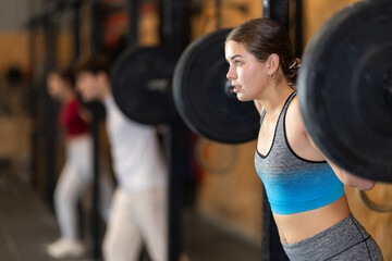 Fototapeta premium Woman in top and leggings doing heavy strength training with a barbell. European woman at a Crossfit group training is preparing to perform lunges and squats