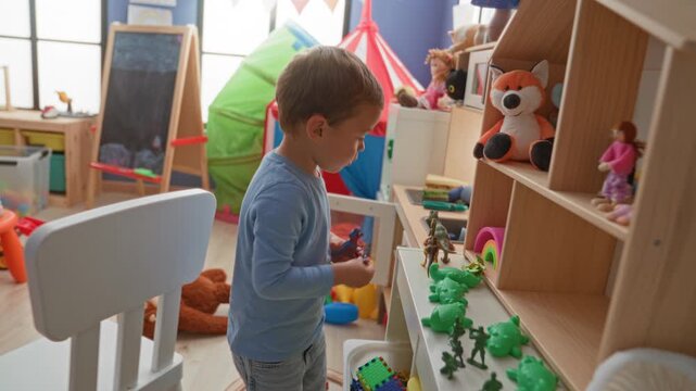 Boy places a toy dinosaur on a low shelf in a playroom inside a building, surrounded by plush fox, rainbow stacker and green frog toys; quiet concentration.