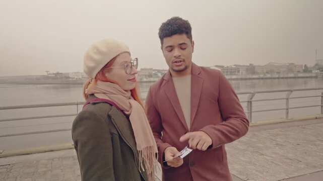 Mixed-race couple pointing directions on a city riverfront promenade