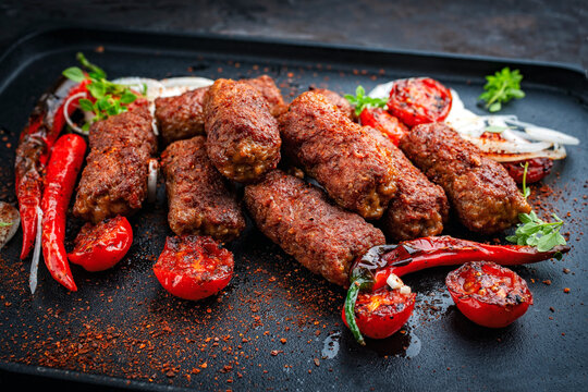 Traditional original artisan grilled cevapi made of spicy minced meat onion, roasted tomato and chili served as close-up on a design plate