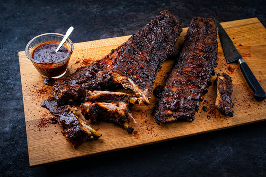 Barbecue spare ribs St Louis baby back cut with homemade artisan hot chili bbq grill sauce dip served as close-up on a wooden cutting board