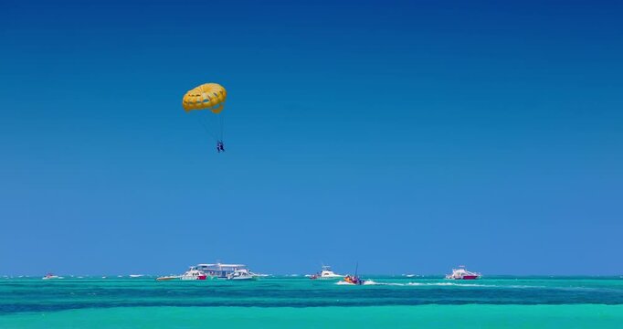 Parasailing with a yellow parachute high in the blue sky over the turquoise Caribbean sea, summer water sport activity 
