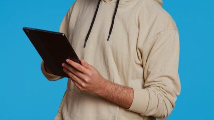 Arab guy using tablet to scroll on online websites, looking for something on the internet and using social media apps. Modern person working with touchscreen device in studio. Camera 2. © DC Studio
