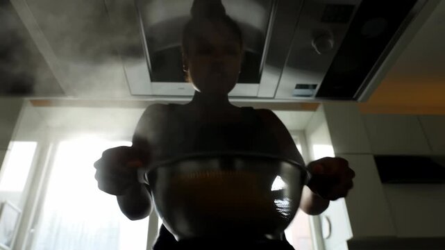 Steaming bowl held by silhouetted cook in kitchen
