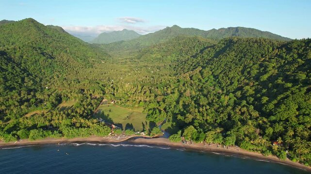 Aerial drone footage of Malimbu beach valley in Pemenang area, Lombok island, Indonesia, with flat quiet blue water, forests and mountains behind, at golden sunset
