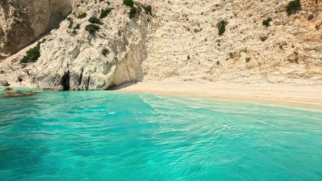 Drone footage departing from a secluded beach with crystal-clear turquoise water and white limestone cliffs on Ithaca Island, Greece. Stunning Ionian Sea coastline showcasing pristine Mediterranean na
