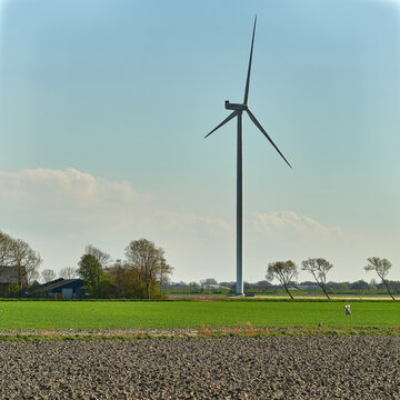 Middenmeer, Netherlands - 14 April 2026: View of a large wind turbine in the Wieringermeer polder with a plowed field in the foreground and farm buildings under a clear sky.
