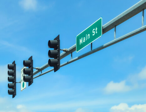 Main Street sign mounted on a metal structure with traffic signals against a clear blue sky background.