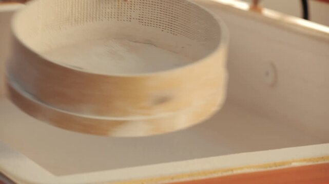 Hands using a wooden sieve to sprinkle protective powder inside a ceramic oven