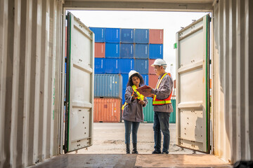 Obraz premium Logistics workers in hard hats and safety vests shake hands among stacked shipping containers at a cargo terminal.