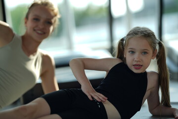 Fototapeta premium Mother and young daughter stretch and exercise together on a mat in a bright gym, sharing a healthy active lifestyle.