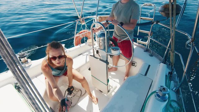 Sailing in the smooth sea during sunny day. Man and woman sail the small sailing boat in the region of the island of Ilha Grande in Brazil