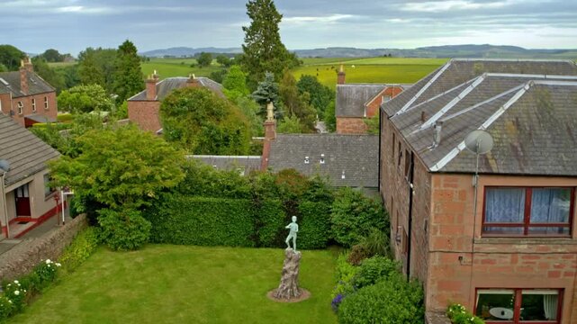 Aerial view flying over a garden with a statue of Peter Pan and revealing the scottish countryside