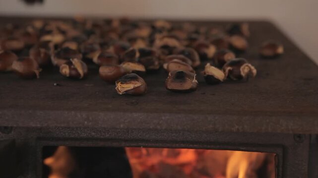 Cozy winter scene showing fresh chestnuts cooking on a hot stove top with a warm crackling fire in the background.